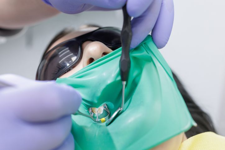 Dentist examining a patient’s open mouth with mirror and probe, wearing blue gloves and safety glasses