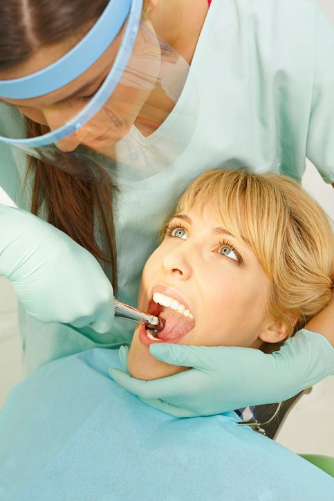 Dentist examining a patient’s mouth with a dental mirror, both wearing protective gloves and masks