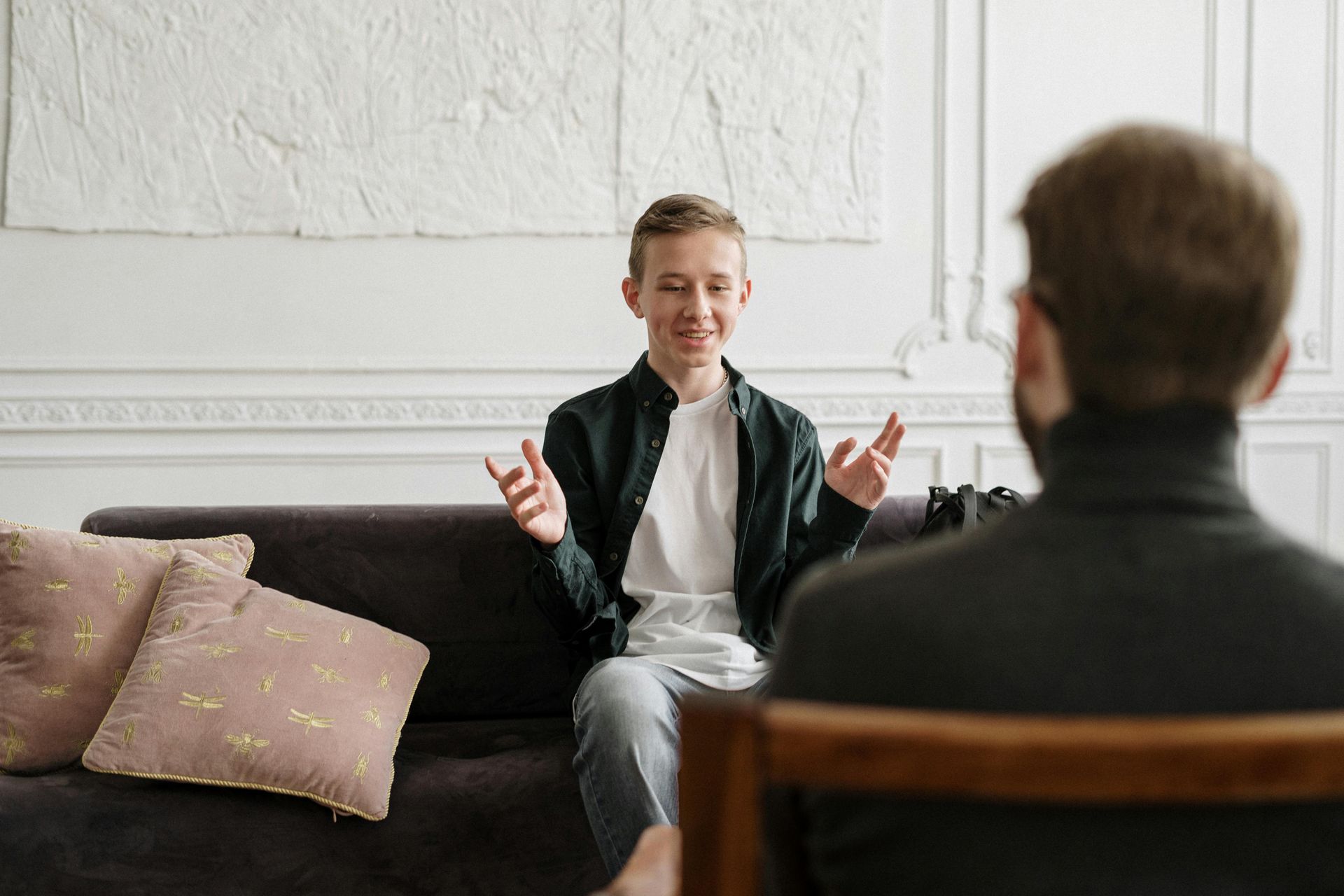Young man smiling, gesturing while talking to person in therapy session.