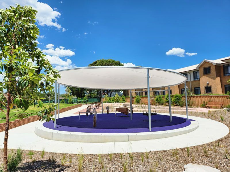 A large white umbrella is sitting on top of a purple circle in a park.