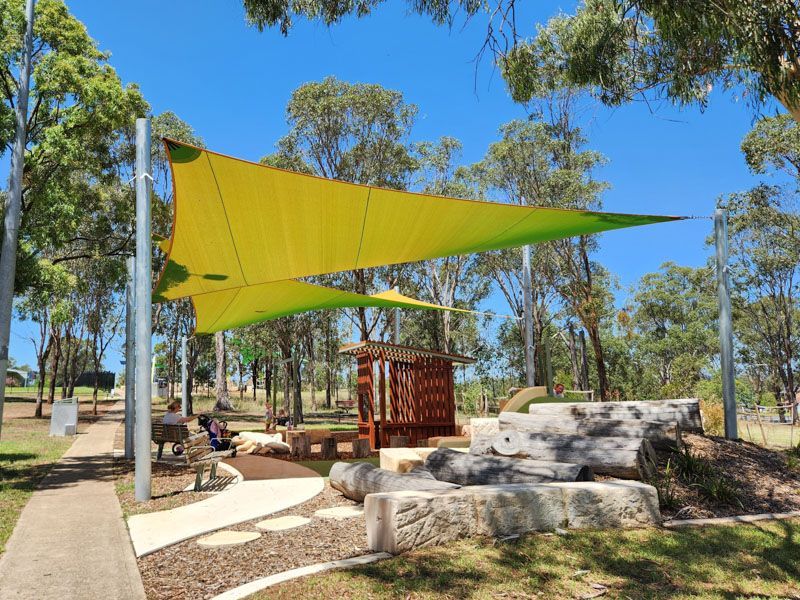 A yellow and green umbrella is hanging over a playground in a park.