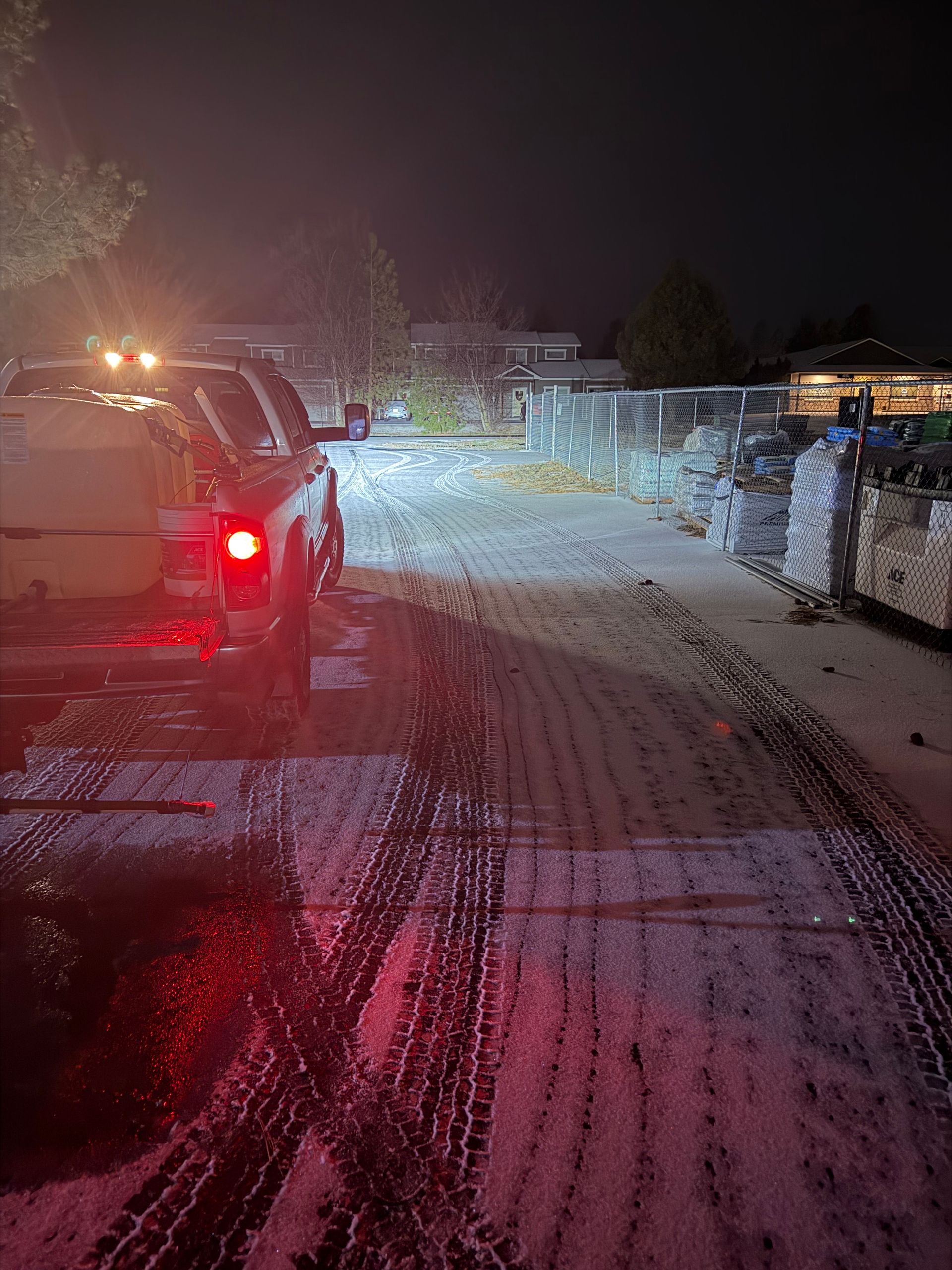 A truck with a tank in the bed parked at night on a snow-covered surface with tire tracks leading forward.