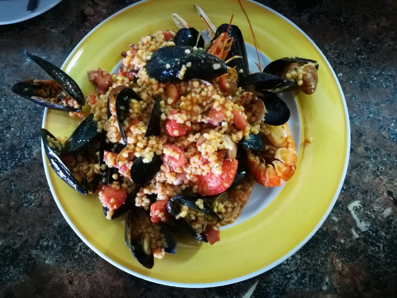 Paella di frutti di mare con cozze, gamberi e riso su un piatto giallo.