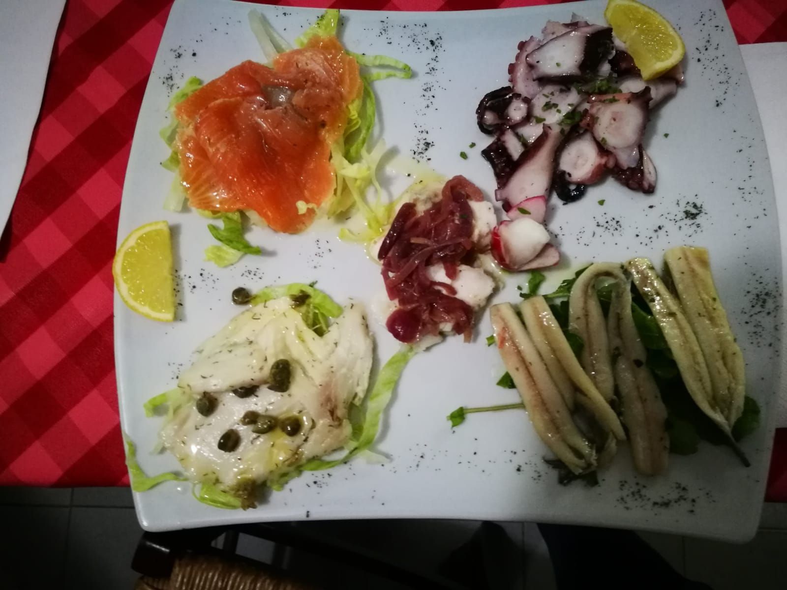 Piatto di frutti di mare: salmone affumicato, polpo, pesce marinato, acciughe e tonno, serviti con limone e lattuga.