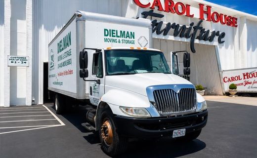 Moving truck parked outside Carol House Furniture store on a sunny day