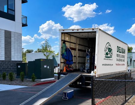 Moving truck with ramp outside a building under a blue sky, with a worker near the open cargo area