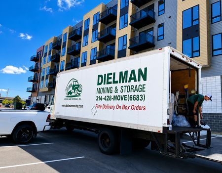 Moving truck with Dielman Moving & Storage logo parked beside a modern apartment building.