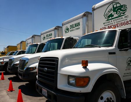 Row of white moving trucks parked by orange cones under a clear blue sky