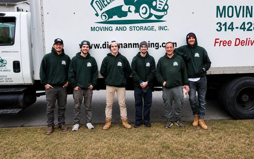 Six workers in dark green hoodies stand in front of a white moving truck.