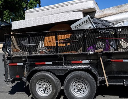 Overloaded trailer carrying furniture, mattresses and boxes behind a black mesh side panel.