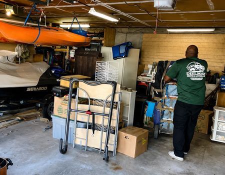 Garage with stacked boxes, hand truck, kayak overhead, and a person organizing items.
