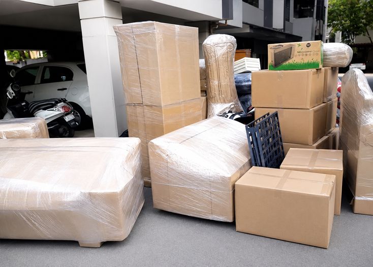 Wrapped furniture and cardboard boxes stacked in a parking area under an overhang