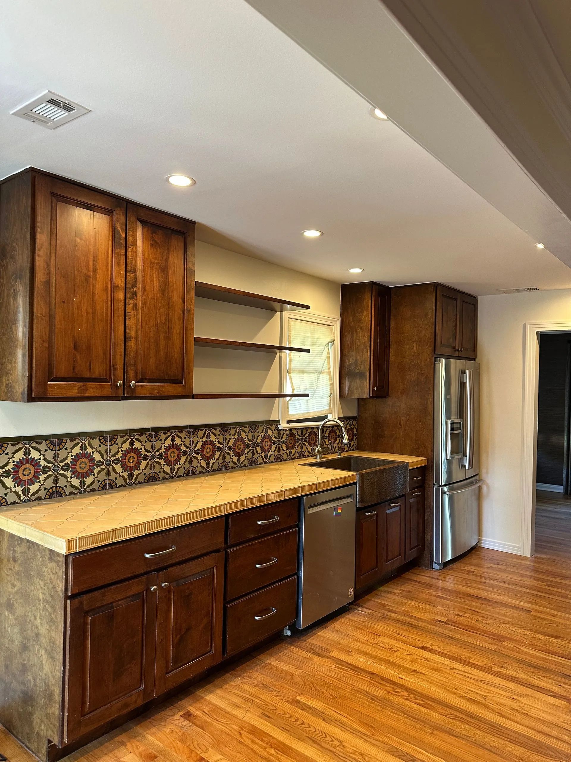 Modern kitchen with dark wood cabinets, granite counters, stainless fridge, and hardwood floor.