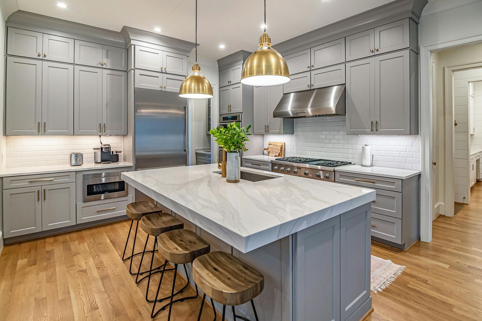 Modern kitchen with gray cabinets, large marble island, brass pendants, and stainless steel appliances.