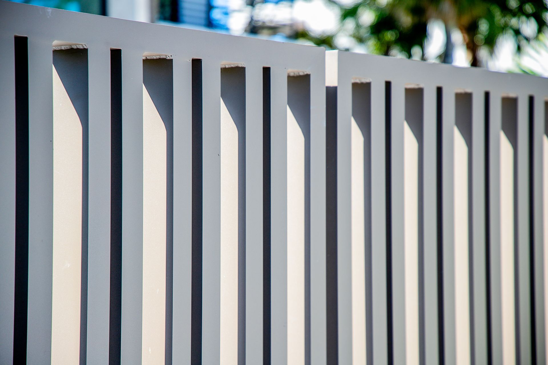 Close-up of a modern, light gray vertical slat fence with clean shadows cast against the panels.