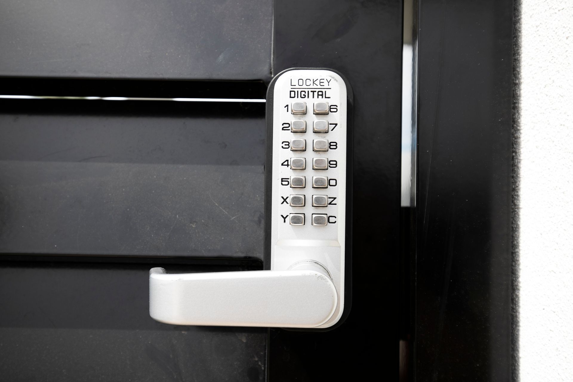 A silver digital keypad door lock with a handle mounted on a black door.