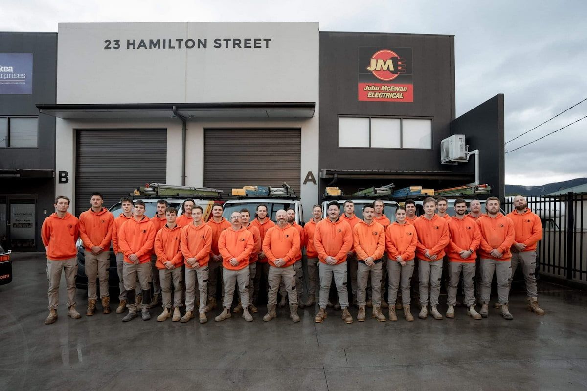 A Group Of Men Are Posing For A Picture In Front Of A Building — John McEwan Electrical In Albion Park, NSW