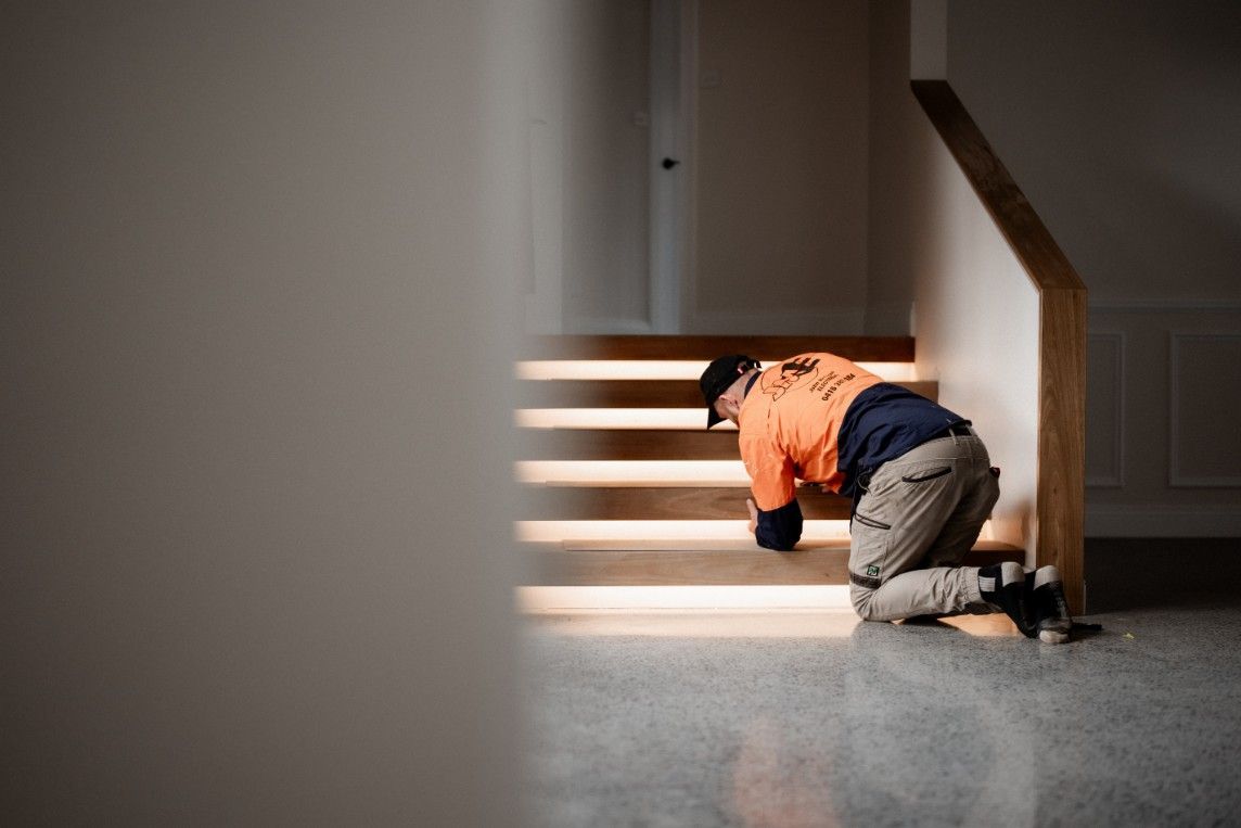 A Man is Kneeling Down on the Floor in Front of a Set of Stairs — John McEwan Electrical in Dapto, NSW