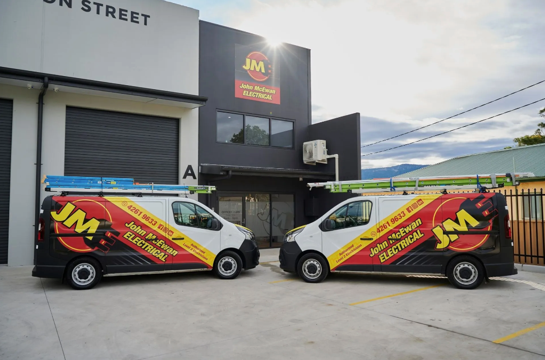 Two branded John McEwan Electrical service vans are parked outside their premises.