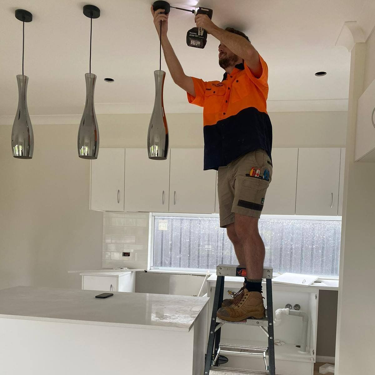 A Man Is Standing On A Ladder Working On A Light Fixture — John McEwan Electrical In Moss Vale, NSW