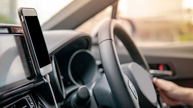 Car dashboard with a smartphone mount and a driver’s hand on the steering wheel