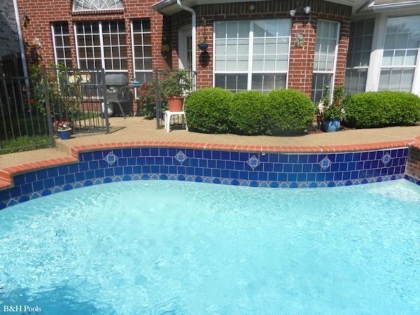 A large swimming pool in front of a brick house