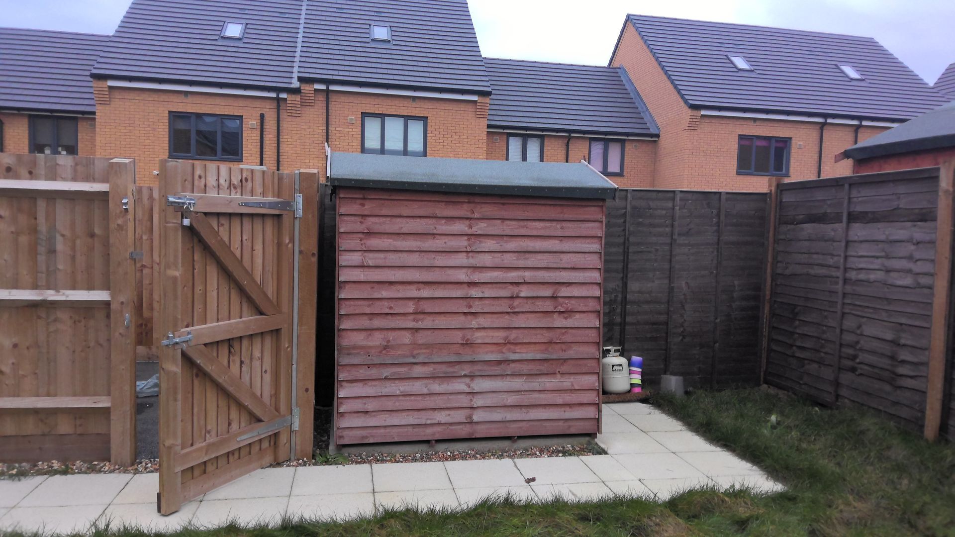 A wooden shed is behind a wooden fence in a backyard.