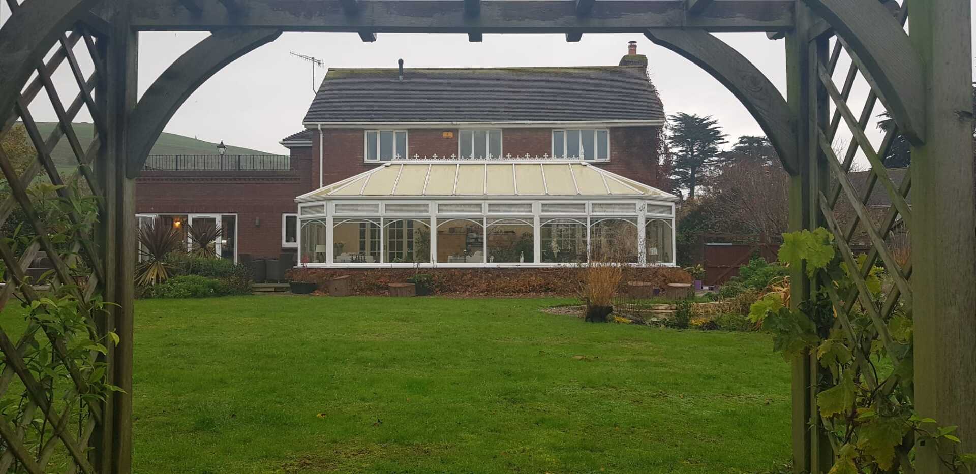A large house with a greenhouse in the backyard is visible through a wooden archway.