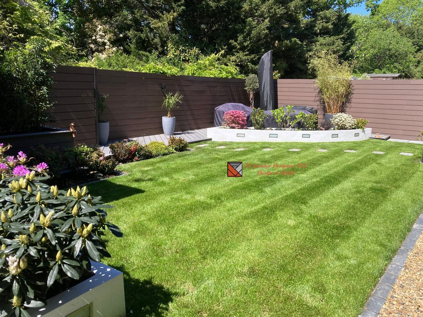 Well-manicured green lawn with striped mowing pattern, stone flowerbed, and brown fence in a sunny garden.