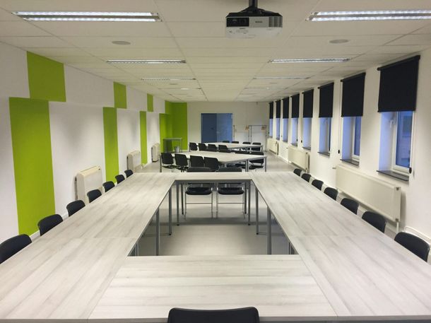 A conference room with tables and chairs and a projector on the ceiling