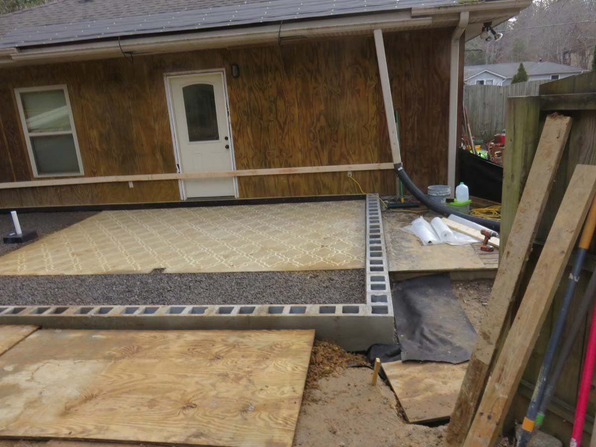 Construction site with a raised plywood deck beside a house, unfinished ramp in front, and stacked materials nearby