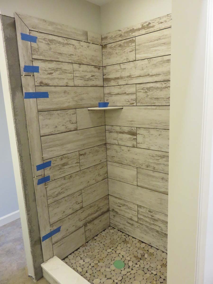 Empty tiled shower stall with beige stone-look walls, pebble floor, and built-in corner shelf.