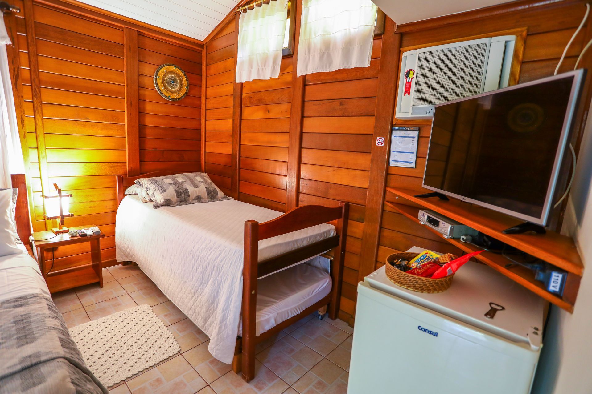Um quarto com cama, televisão, geladeira e ar condicionado.