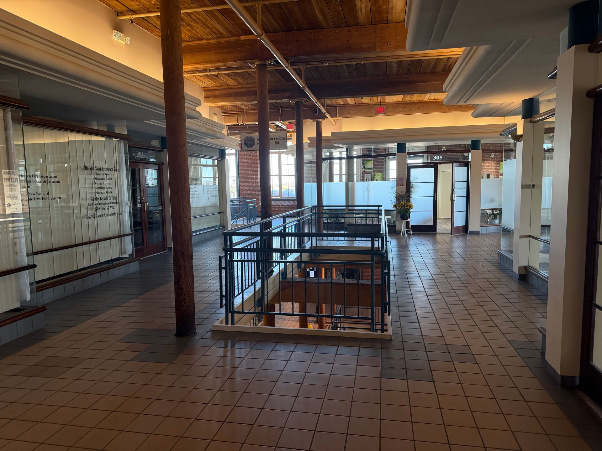 Empty loft-style office with brick floor, exposed beams, and glass partitions