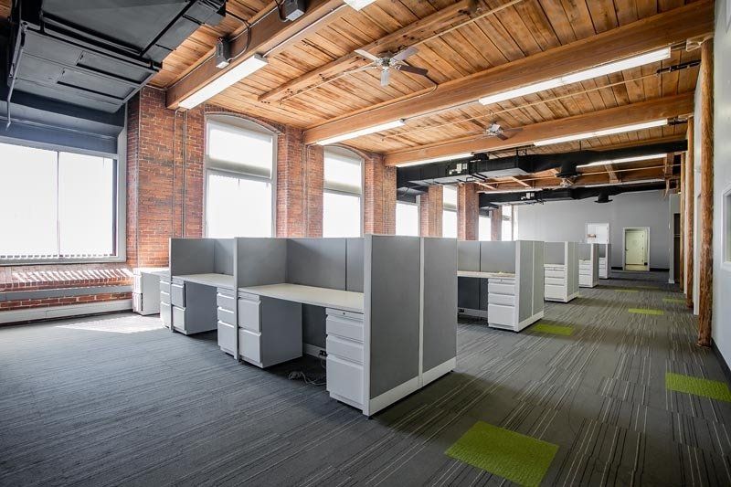 Open office with gray cubicles, wooden ceiling, and large windows