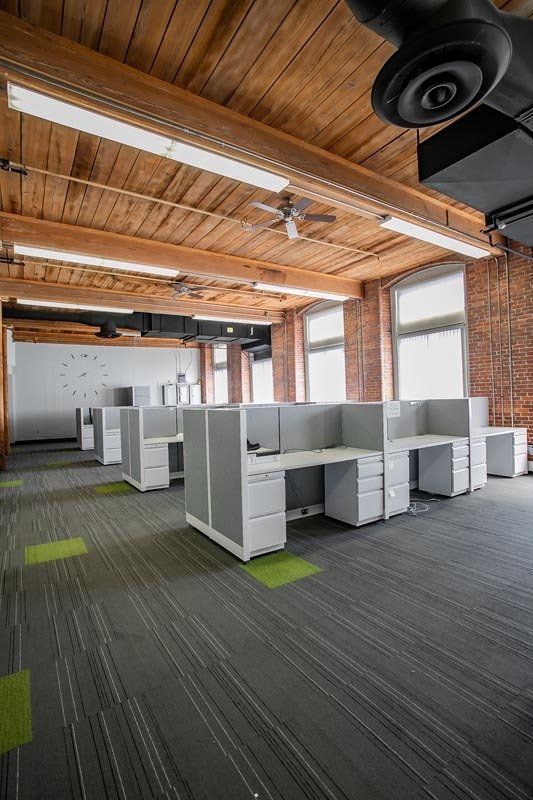 Empty modern office with white cubicles, exposed wood beams, and large windows
