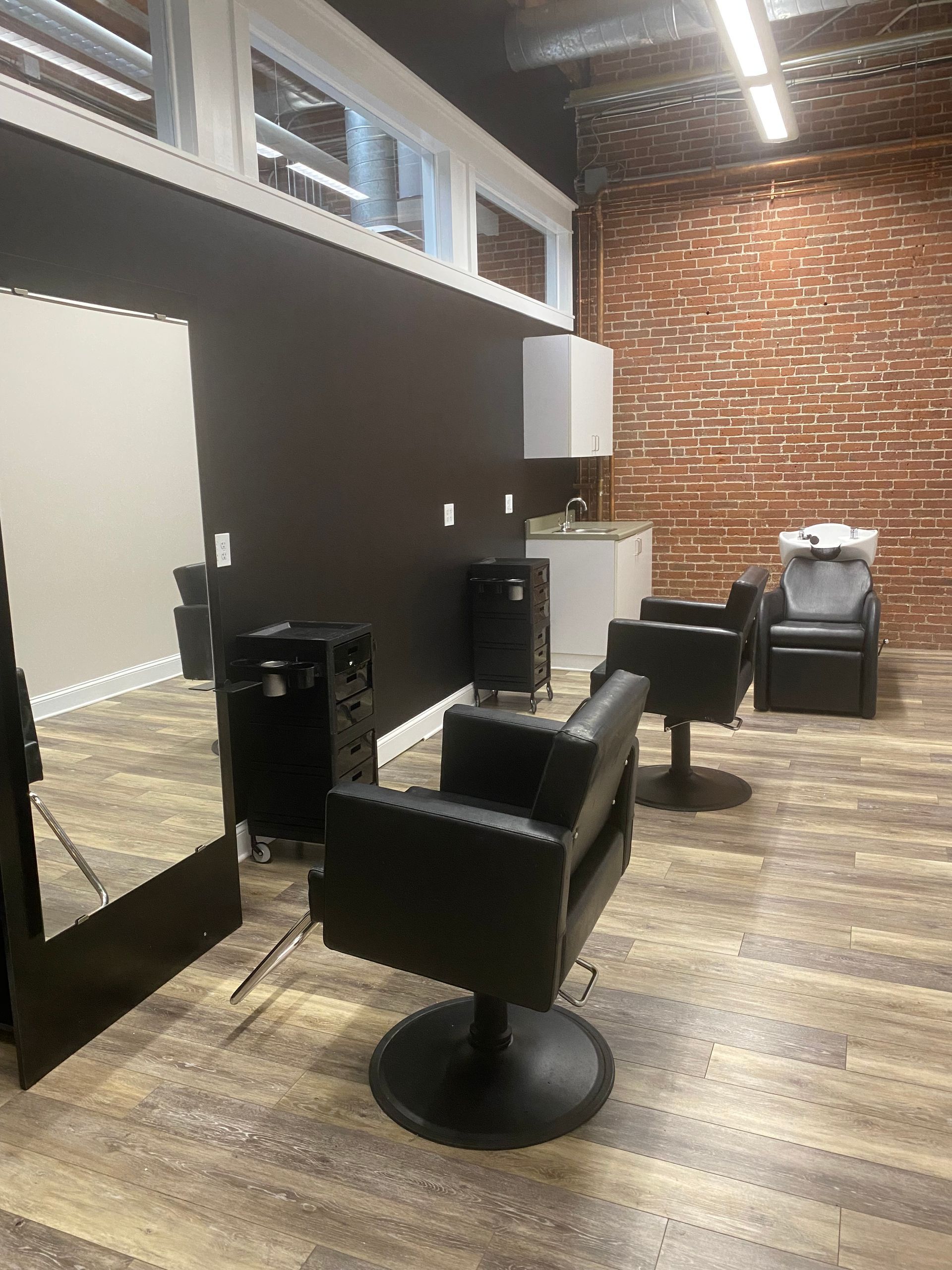 Empty modern salon with black chairs, mirrors, and brick accent wall