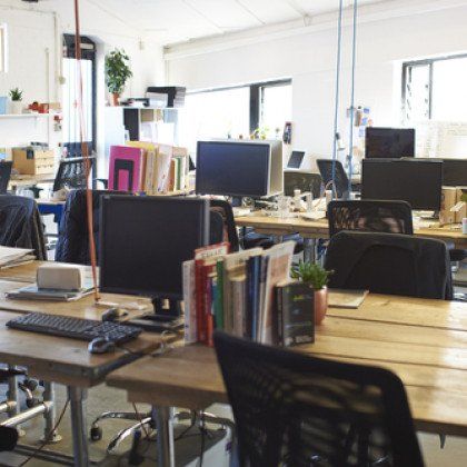 Open office workspace with desks, computers, chairs, and books in a bright room