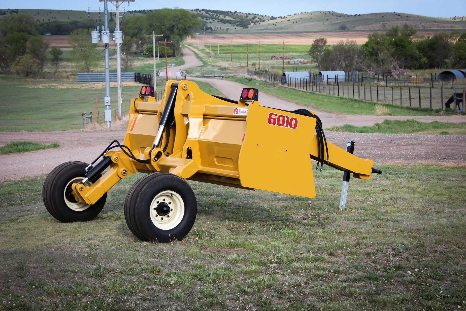 A yellow scraper is parked in a grassy field.