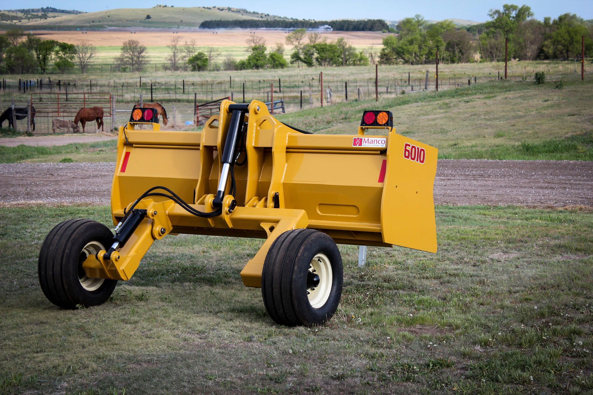 A yellow scraper is parked in a grassy field.
