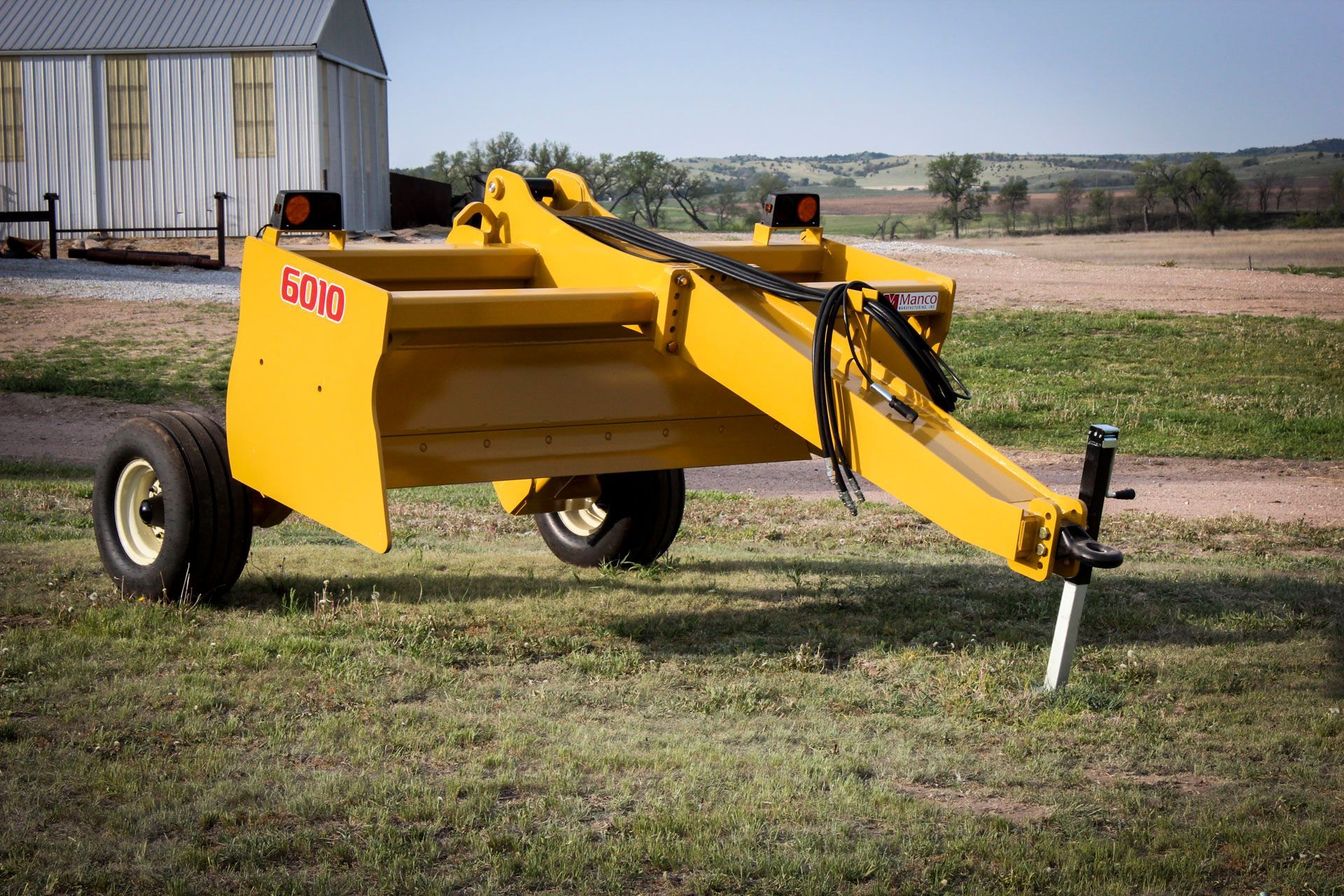 A yellow scraper is parked in a grassy field.