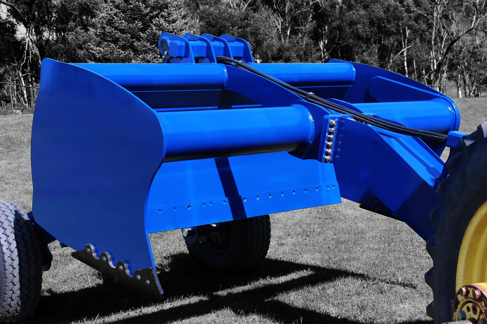A blue scraper is parked in a grassy field