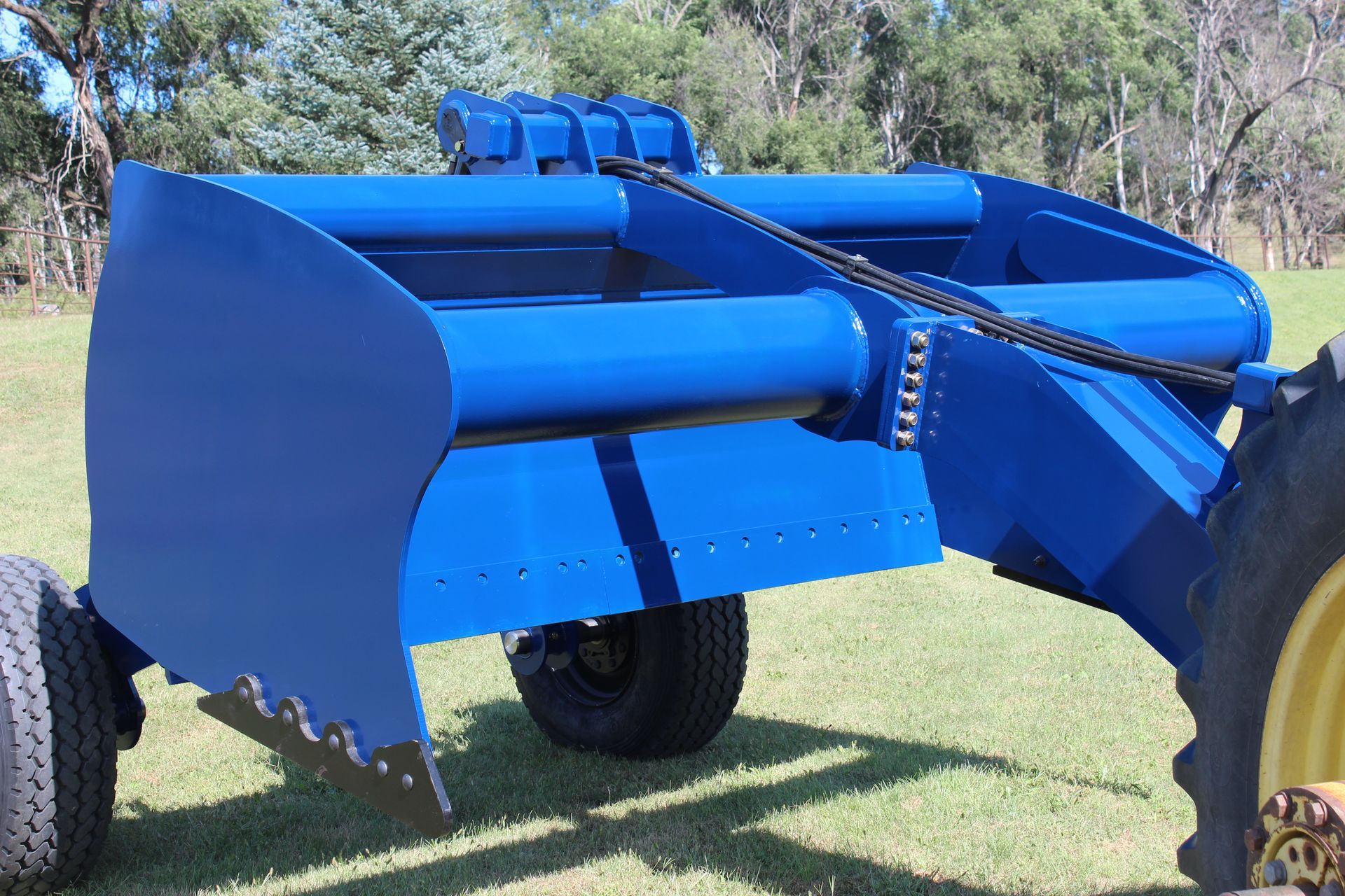 A blue scraper is parked in a grassy field