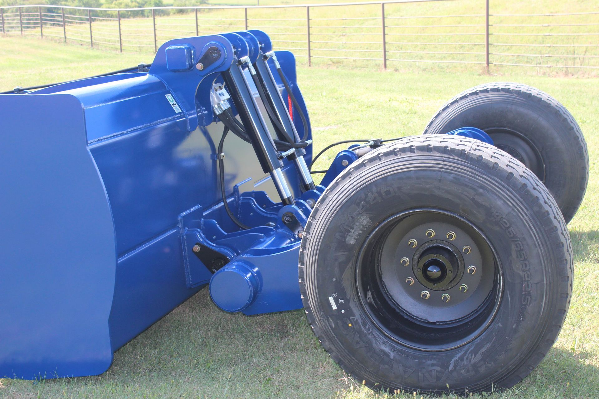 A blue scraper is parked in a grassy field.