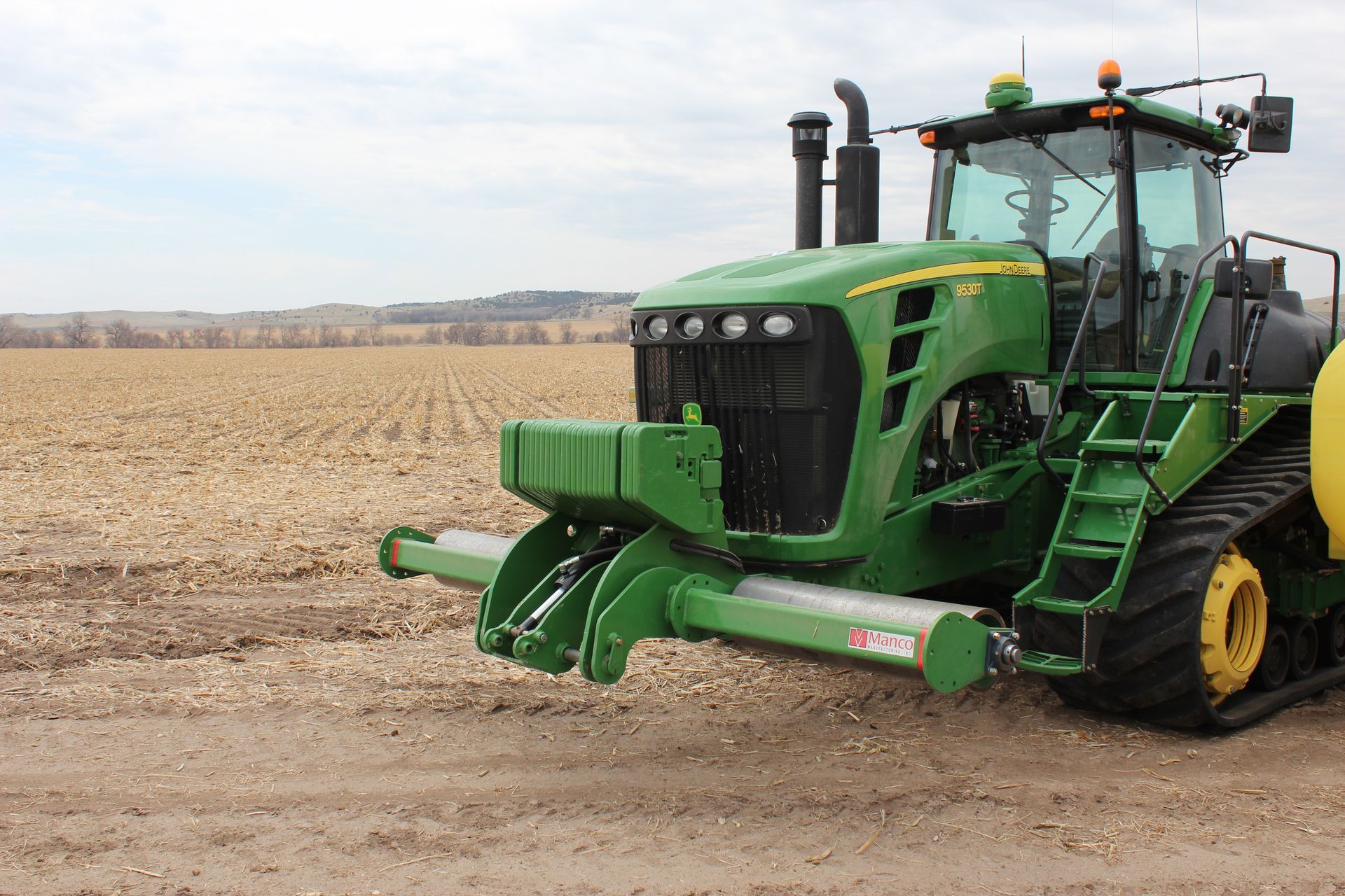 A green john deere tractor with a stalk roller