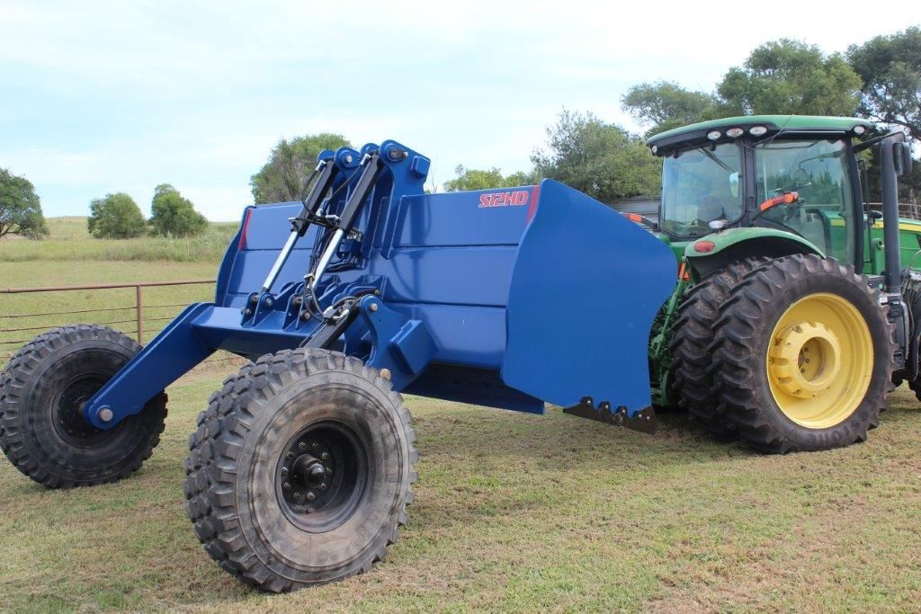 A blue and yellow tractor with a scraper is parked in a grassy field.