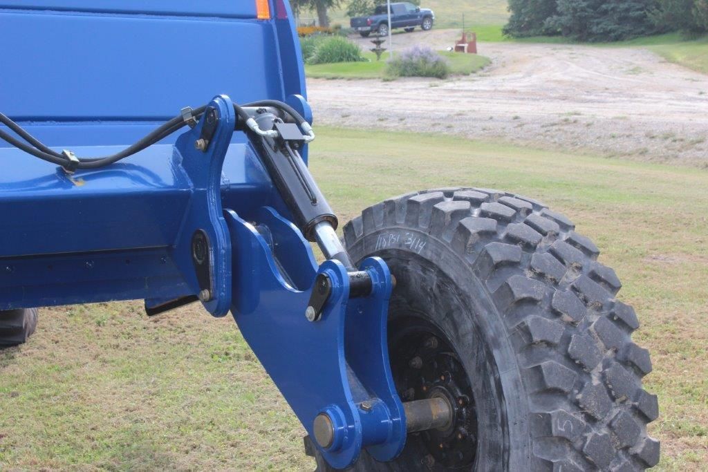 A blue scraper with a large tire is parked in a grassy field.