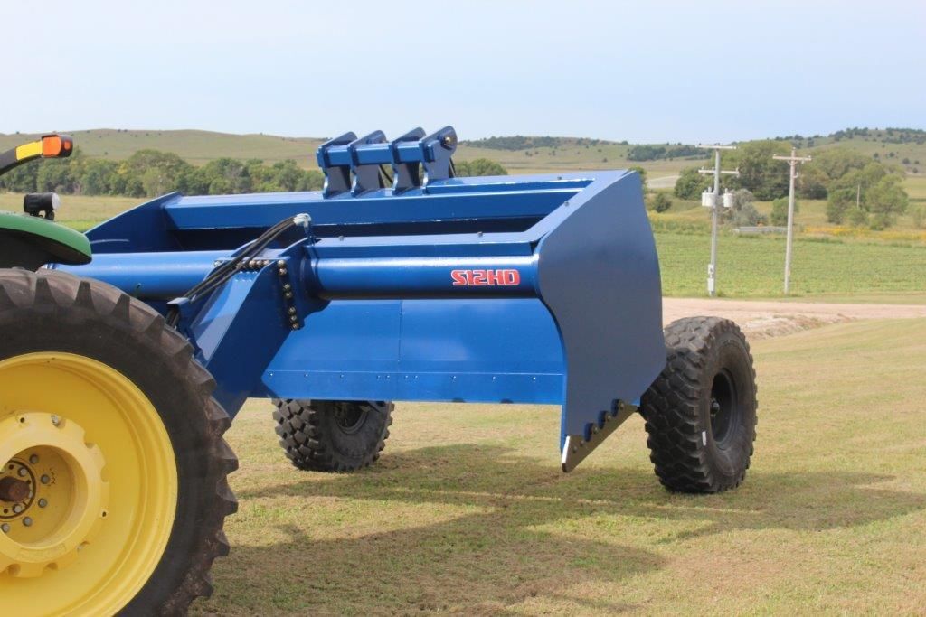 A blue scraper is attached to a tractor