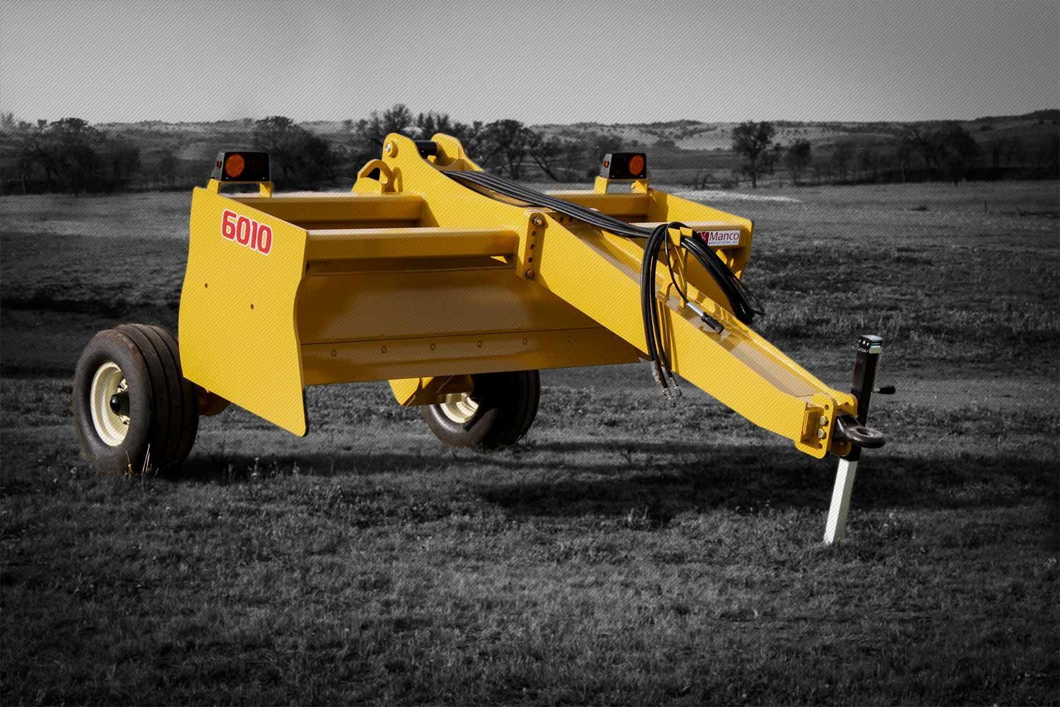 A yellow scraper is parked in a grassy field.
