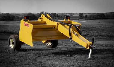 A yellow scraper with the word gono on the side is parked in a field.